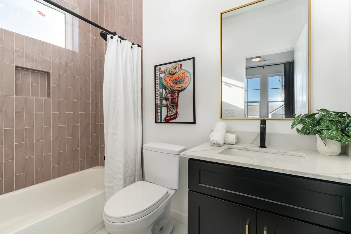A bright bathroom scene featuring framed artwork, a mirror, sink, toilet, and a shower curtain hinting at a tub/shower combo. The space is fresh and inviting, designed for both relaxation and daily routines.
