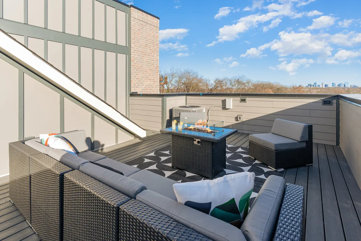 An inviting outdoor seating area on a rooftop, complete with plush lounge furniture, a central coffee table, and sweeping views of the Nashville skyline beyond. The setting is designed for casual socializing, relaxing at sunset, or enjoying drinks and conversation under starry skies.