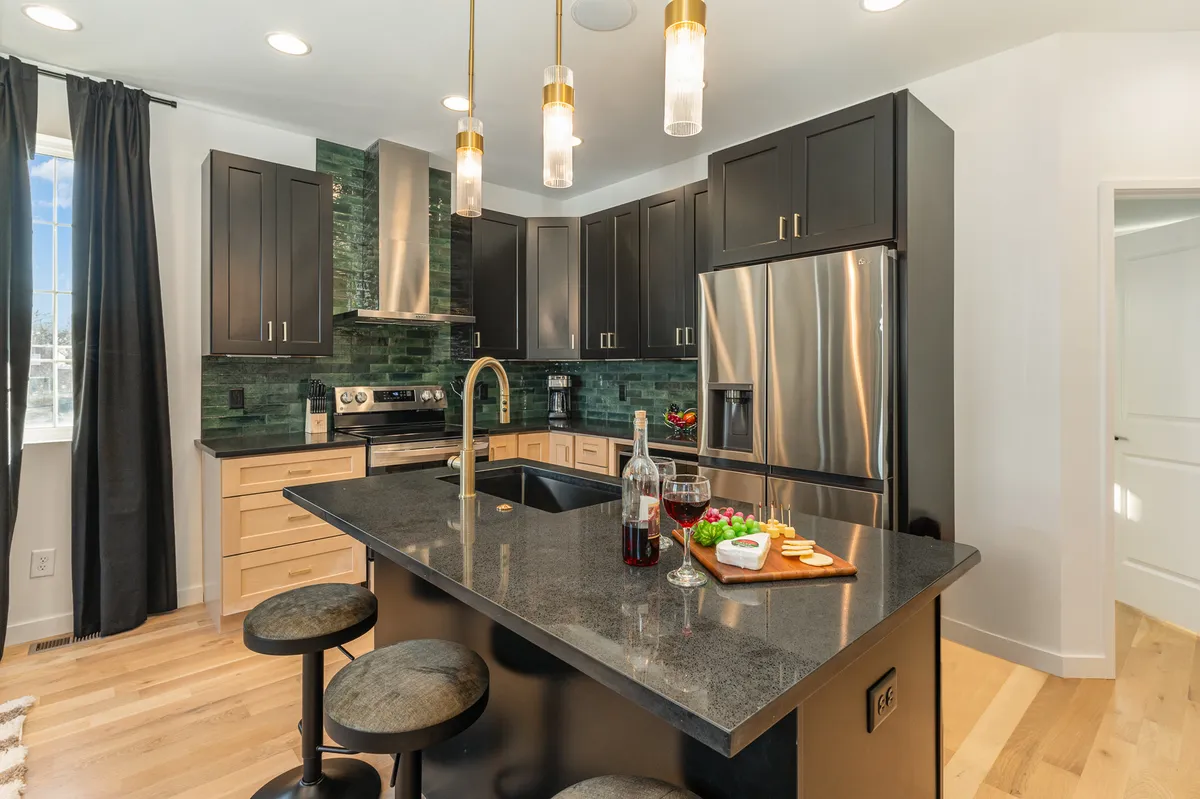 A view of the modern kitchen features a generous island countertop with bar seating for three, contemporary lighting fixtures, and high-end stainless steel appliances. The space feels bright and inviting, with clean lines and a welcoming ambiance for both cooking and socializing.