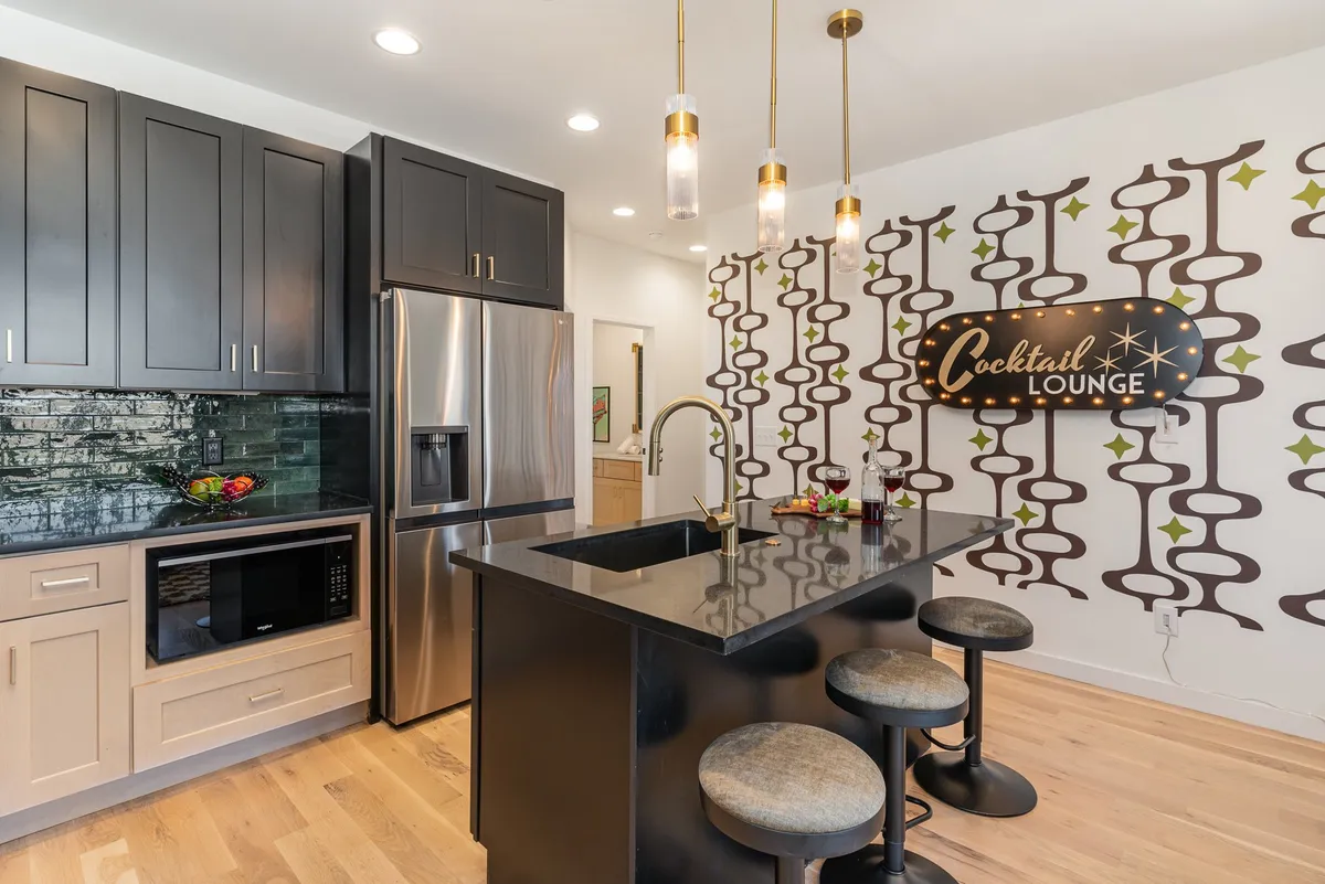 A stylish bar lounge area featuring a black granite countertop, distinctive 'Cocktail Lounge' signage, chic bar stools, and a decorative patterned wall. The setting is playful, modern, and primed for entertaining and socializing with friends or family.